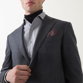 Model wearing Corneliani Flannel Two-Piece Suit in grey wool, styled with a check shirt, black turtleneck, and burgundy pocket square.