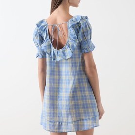 Model wearing Damson Madder Harlow Check Mini Dress in blue check, showing scoop back with self-tie fastening, ruffle trim and short sleeves