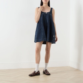 Model wearing Damson Madder Immy Denim Mini Dress in blue with square neckline and pleated detail, styled with white socks and brown loafers