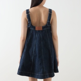 Model wearing Damson Madder Immy Denim Mini Dress in blue, back view showing logo badge, adjustable straps and white contrast stitching