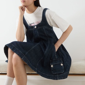 Model wearing Damson Madder Immy Denim Mini Dress in blue with adjustable straps, patch pocket, and pleated details, styled with a white graphic tee