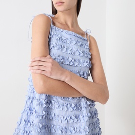Model wearing Damson Madder blue cotton mini dress with textured ruffle tiers and tie shoulder straps, cropped view.