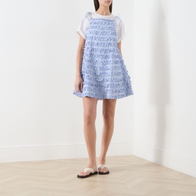 Model wearing Damson Madder blue textured ruffle cotton mini dress, styled with a white T-shirt and silver flat sandals.