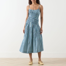 Model wearing Damson Madder Lyra Panelled Tomboy Check Dress in blue check, midi length with flared skirt and adjustable straps. Styled with yellow