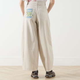 Model wearing Damson Madder Erika Barrel Leg Jeans in stone, wide barrel-leg silhouette with branded graphic patch on rear pocket.