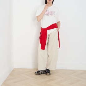 Model wearing Damson Madder Erika Barrel Leg Jeans in stone, styled with a white graphic tee and red sweatshirt tied at the waist.