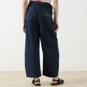 Model wearing Damson Madder Augusta Mid-Rise Straight Leg Jeans in dark indigo with frill tie waist detail, wide straight legs and rear patch pocket.