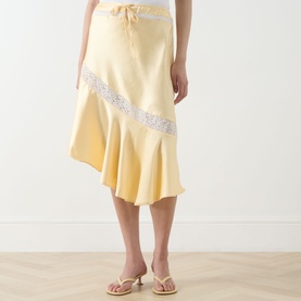 Model wearing Damson Madder Delphia Embellished Skirt in yellow satin with diagonal lace trim, asymmetric hem and drawstring waist, styled with gold