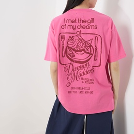 Model wearing Damson Madder Gill Of Dreams Graphic T-Shirt in pink, showing back graphic print, styled with navy wide-leg trousers.