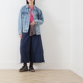 Model wearing Damson Madder Gill Of Dreams Graphic T-Shirt in pink, styled with denim jacket, navy wide-leg trousers and chunky boots.