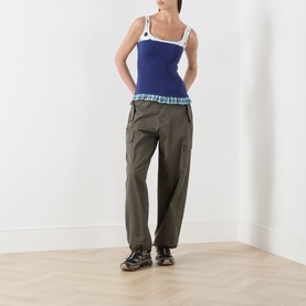 Model wearing Damson Madder navy cotton tank top with white trim, styled with khaki cargo trousers and dark trainers.