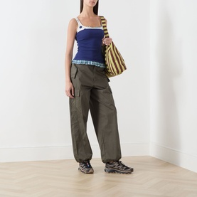 Model wearing Damson Madder navy cotton top with olive cargo trousers, chunky trainers, and a striped shoulder bag.