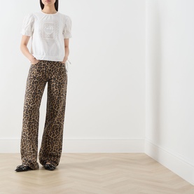 Model wearing Damson Madder white cotton top with puff sleeves and graphic print, styled with leopard print wide-leg trousers and black loafers.