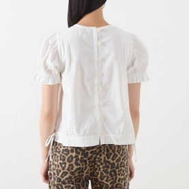Model wearing Damson Madder white cotton top, back view showing button placket, puff sleeves with tie detail, styled with leopard print trousers.