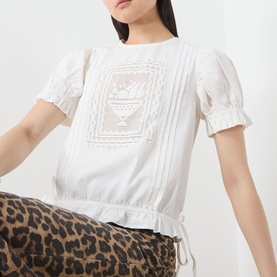 Model wearing Damson Madder white cotton top with puff sleeves, pintuck detail and embroidered panel, styled with leopard-print trousers.