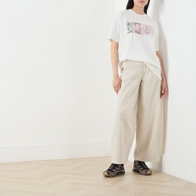Model wearing Damson Madder off white cotton graphic T-shirt, styled with wide-leg beige trousers and dark chunky trainers.