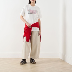 Model wearing Damson Madder off white graphic cotton T-shirt, styled with red top tied at waist and wide-leg beige trousers.