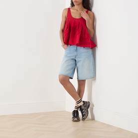 Model wearing Damson Madder Stella Ruffle Cami in red with light blue denim bermuda shorts and black lace-up boots.