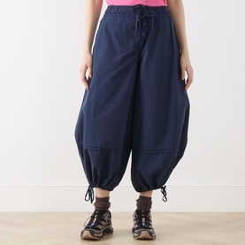 Model wearing Damson Madder Frida Bloomer Trousers in navy, with elasticated waist and gathered cuffs, styled with hiking shoes.