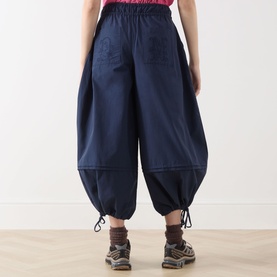 Model wearing Damson Madder Frida Bloomer Trousers in navy, showing rear patch pockets and adjustable drawstring cuffs, styled with hiking boots.
