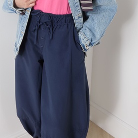 Model wearing Damson Madder Frida Bloomer Trousers in navy with elasticated drawstring waist, styled with a pink top and denim jacket.