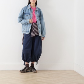 Model wearing Damson Madder Frida Bloomer Trousers in navy, styled with a light wash denim jacket, pink top, and chunky trainers.