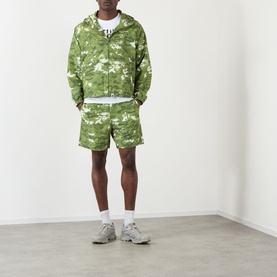 Model wearing BAPE Pixelated Camo Print Logo Windbreaker in green, styled with matching camo shorts and grey trainers.
