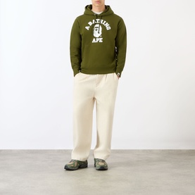 Model wearing olive green A BATHING APE graphic hoodie with white ape logo, styled with cream wide-leg trousers and camo trainers.