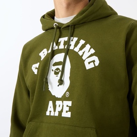Model wearing olive green A Bathing Ape hoodie with white college-style logo graphic and kangaroo pocket