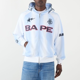 Model wearing BAPE Hand Drawn Football Zip Hoodie in white with bold logo print and zip fastening, styled with blue jeans.