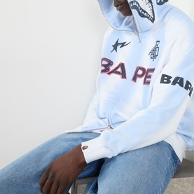 Model wearing BAPE Hand Drawn Football Zip Hoodie in white with logo graphic print, styled with light blue jeans.