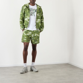 Model wearing BAPE Multi Pixel Camouflage Shorts in green, styled with matching camo zip hoodie, white graphic tee and grey trainers.