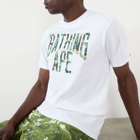 Model wearing BAPE Camouflage NYC Logo T-Shirt in white with green camo logo print, styled with matching camo shorts.