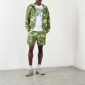 Model wearing BAPE Camouflage NYC Logo T-Shirt in white, styled with matching green camo zip hoodie and shorts, white socks, grey trainers.