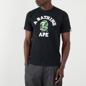 Model wearing BAPE ABC Camouflage College Logo Shirt in black with green camo print logo, styled with grey shorts.