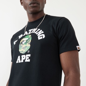 Model wearing BAPE ABC Camouflage College Logo Shirt in black with green camo ape motif print. Gold chain necklace visible.