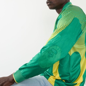 Model wearing BAPE Logo Football Jersey Long-Sleeved T-Shirt in green with yellow dot-print panels and embroidered logo detail.