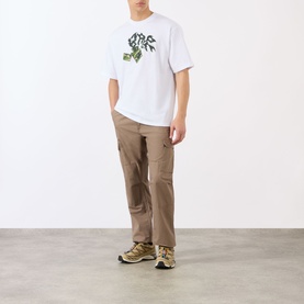 Model wearing BAPE Lighter Relaxed Fit T-Shirt in white with green graphic, styled with tan cargo trousers and gold trainers.