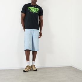 Model wearing BAPE Groovy Justice Logo T-Shirt in black with neon green graphic, styled with light blue denim shorts and gold trainers.