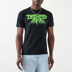 Model wearing BAPE Groovy Justice Logo T-Shirt in black with green graphic Justice League lettering, styled with a chain necklace and light blue