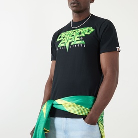 Model wearing BAPE Groovy Justice Logo T-Shirt in black with green graphic lettering, styled with light blue jeans and a green jacket tied at the