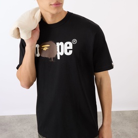Model wearing BAPE Graffiti Logo Relaxed Fit T-Shirt in black with crew neck, holding a plush toy over shoulder.