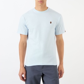Model wearing BAPE One Point Logo T-Shirt in light blue with crew neck, short sleeves, and small logo patch on chest, styled with grey trousers.