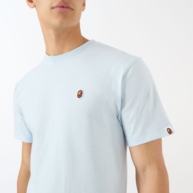Model wearing BAPE One Point Logo T-Shirt in light blue with small ape head logo patch on chest and crew neckline.