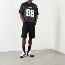 Model wearing BAPE Logo Football Jersey T-Shirt in black with number 88, styled with black shorts and monochrome trainers.
