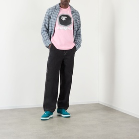 Model wearing BAPE Spray Ape Head Logo T-Shirt in pink, styled with grey check overshirt, black wide-leg trousers and teal trainers.