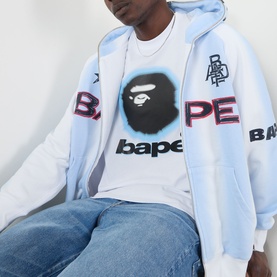 Model wearing BAPE Spray Ape Head Logo T-Shirt in white, styled with a light blue zip-up hoodie and blue jeans.