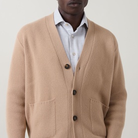 Model wearing Eleventy camel wool-cashmere cardigan with brown buttons and front pockets, styled with a light blue shirt underneath.