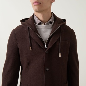 Model wearing Eleventy brown wool jacket with detachable hood and drawstring detail, styled over grey hoodie and checked shirt.