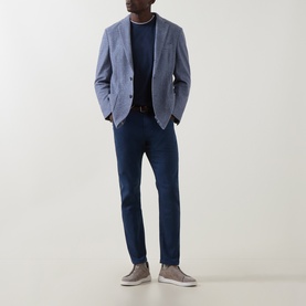 Model wearing Eleventy blue jeans styled with a light blue blazer, navy crewneck, and grey slip-on shoes.
